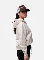Person wearing a beige hoodie and brown cap with 'drop' logo on a white background