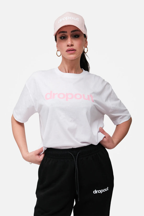 Person wearing a white 'dropout' t-shirt and black pants with a pink cap on a white background