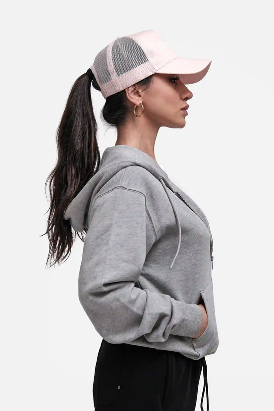 Woman wearing a grey hoodie and pink cap on a white background