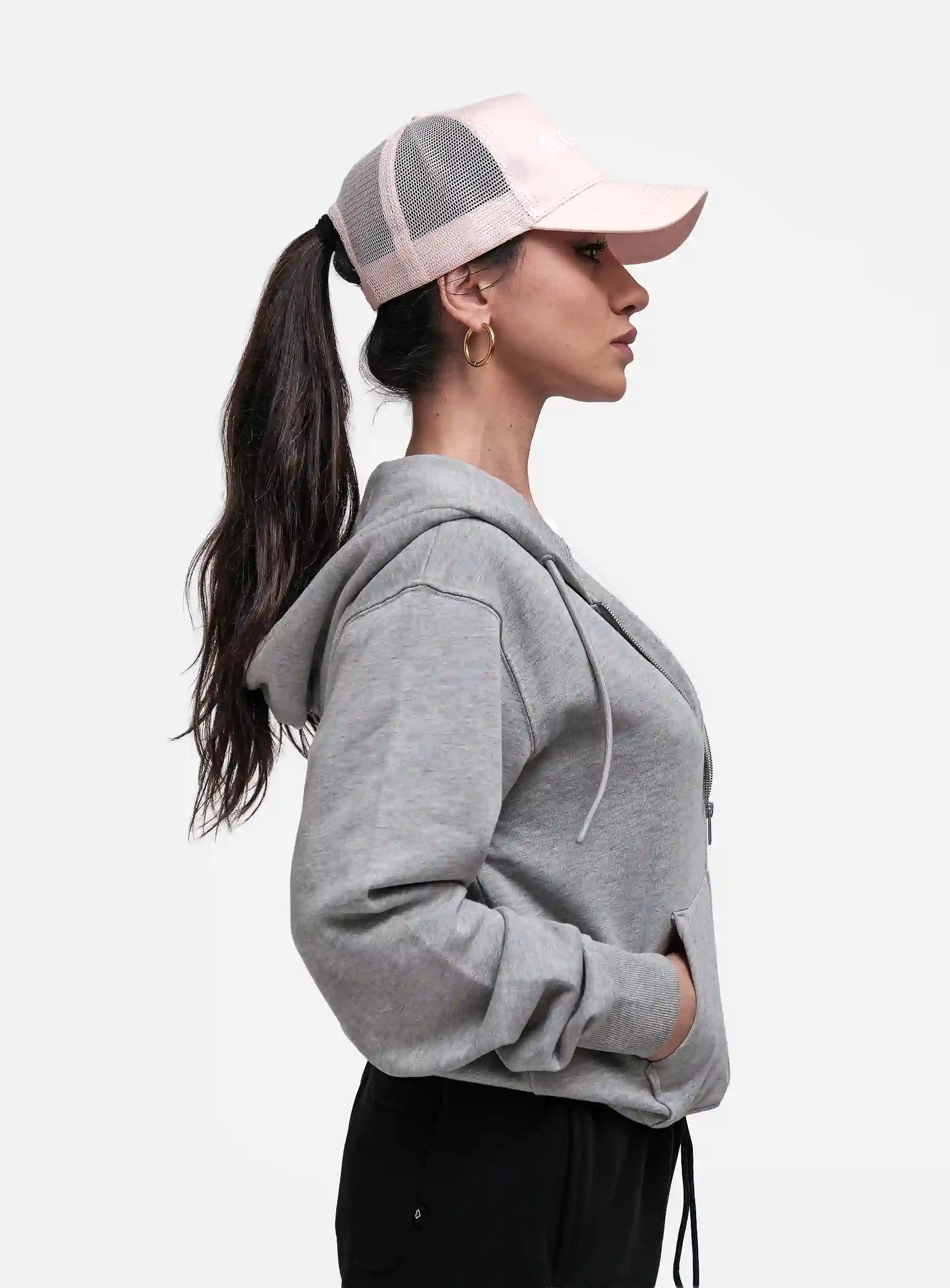 Woman wearing a grey hoodie and pink cap on a white background