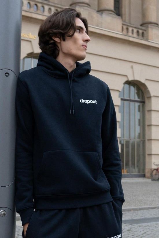 Person wearing a navy hoodie with 'dropout' logo standing against a building.