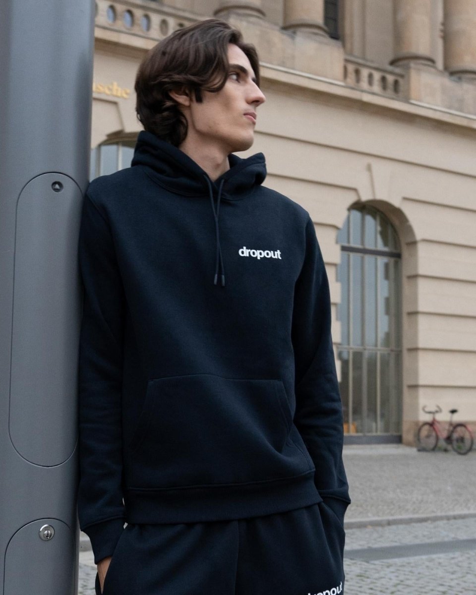 Person wearing a navy hoodie with 'dropout' logo standing against a building.