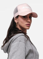 Woman in a pink mesh trucker cap with dropout text and grey hoodie, streetwear style