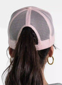 Back view of a woman wearing a light pink mesh trucker hat with a ponytail and hoop earrings
