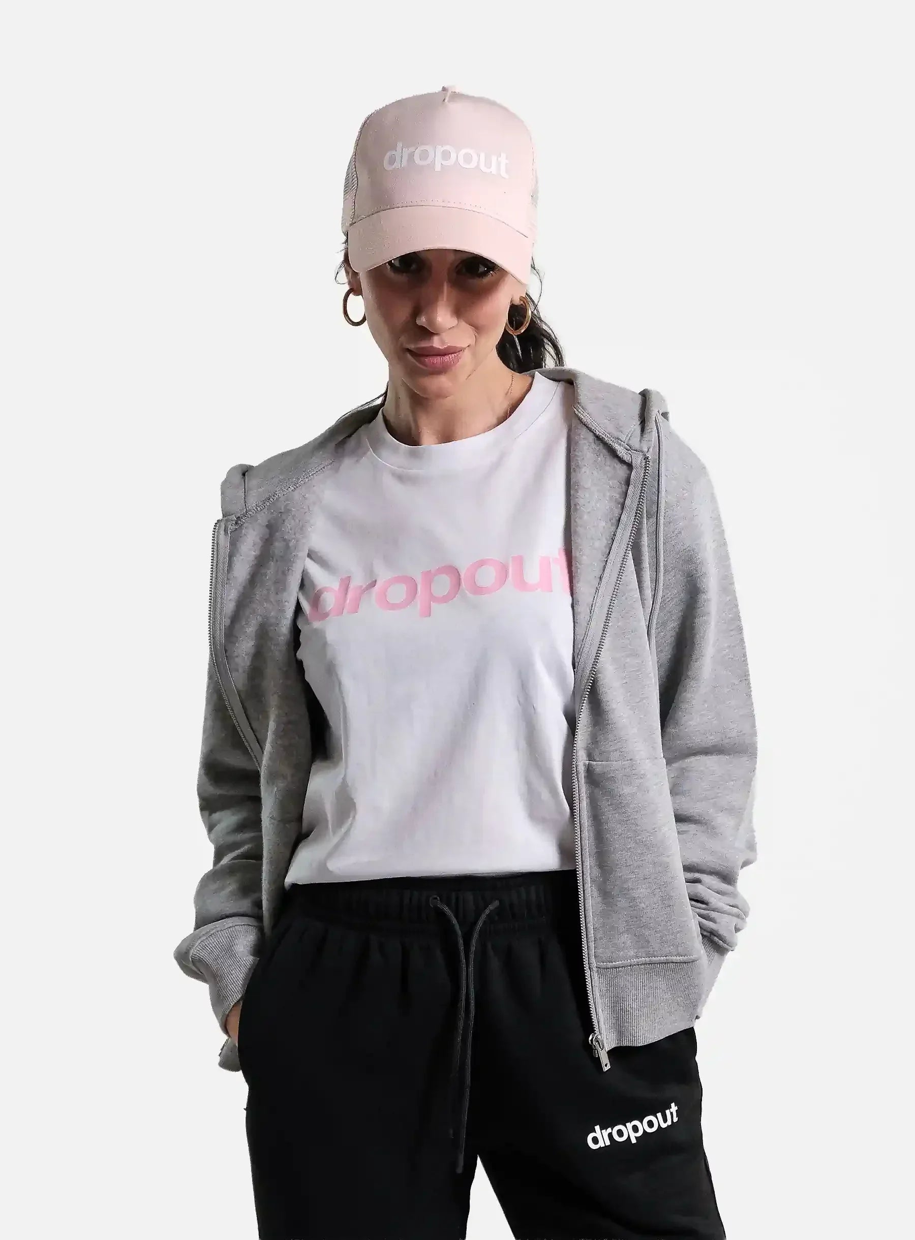 Person wearing a grey hoodie, white t-shirt, black pants, and pink cap with 'dropout' branding on a white background.