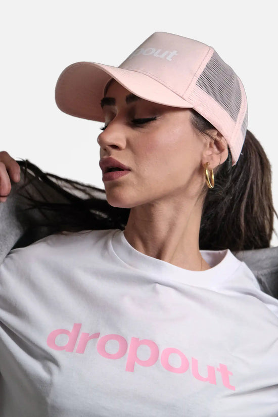 Woman wearing a pink 'dropout' cap and white t-shirt with pink text on a light gray background