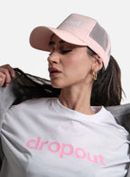 Woman wearing a pink 'dropout' cap and white t-shirt with pink text on a light gray background