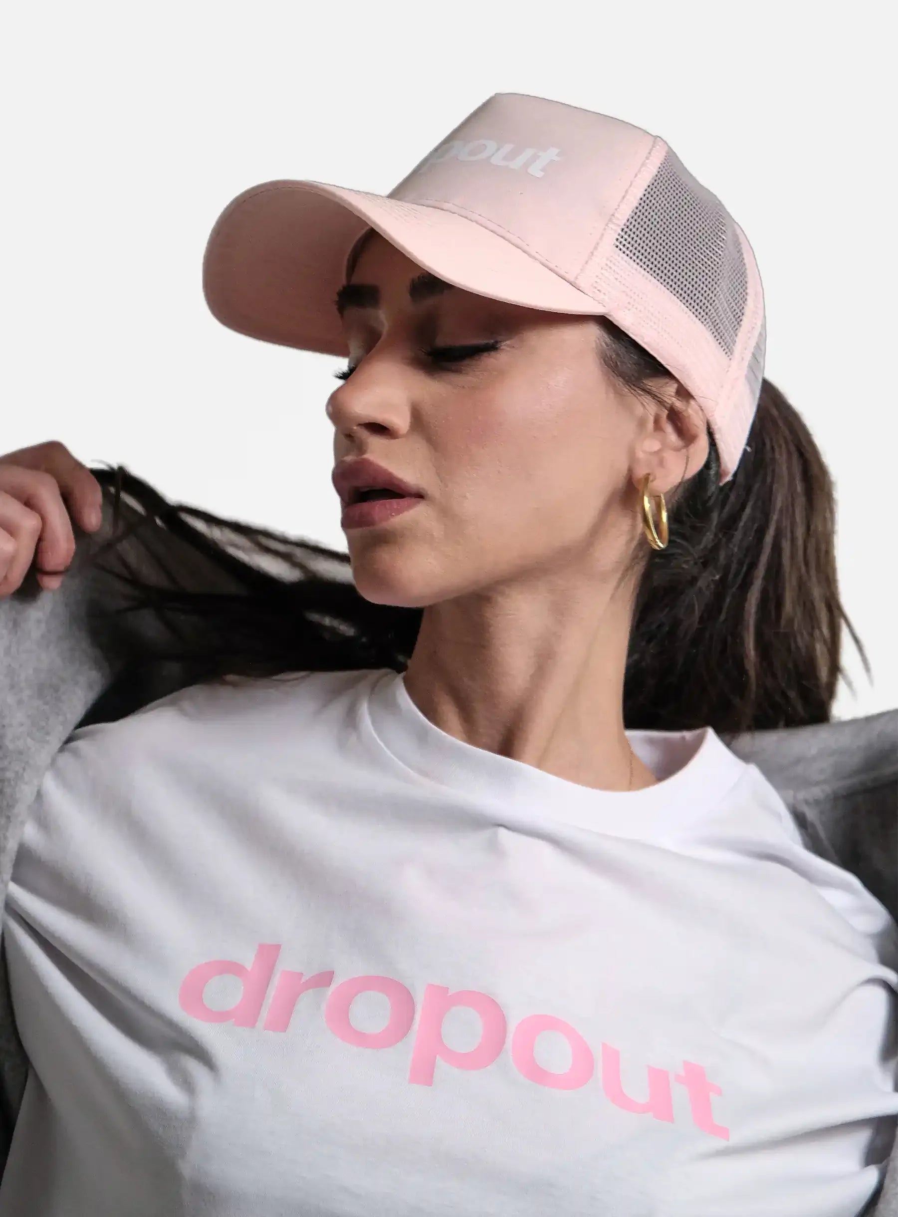 Woman wearing a pink 'dropout' cap and white t-shirt with pink text on a light gray background