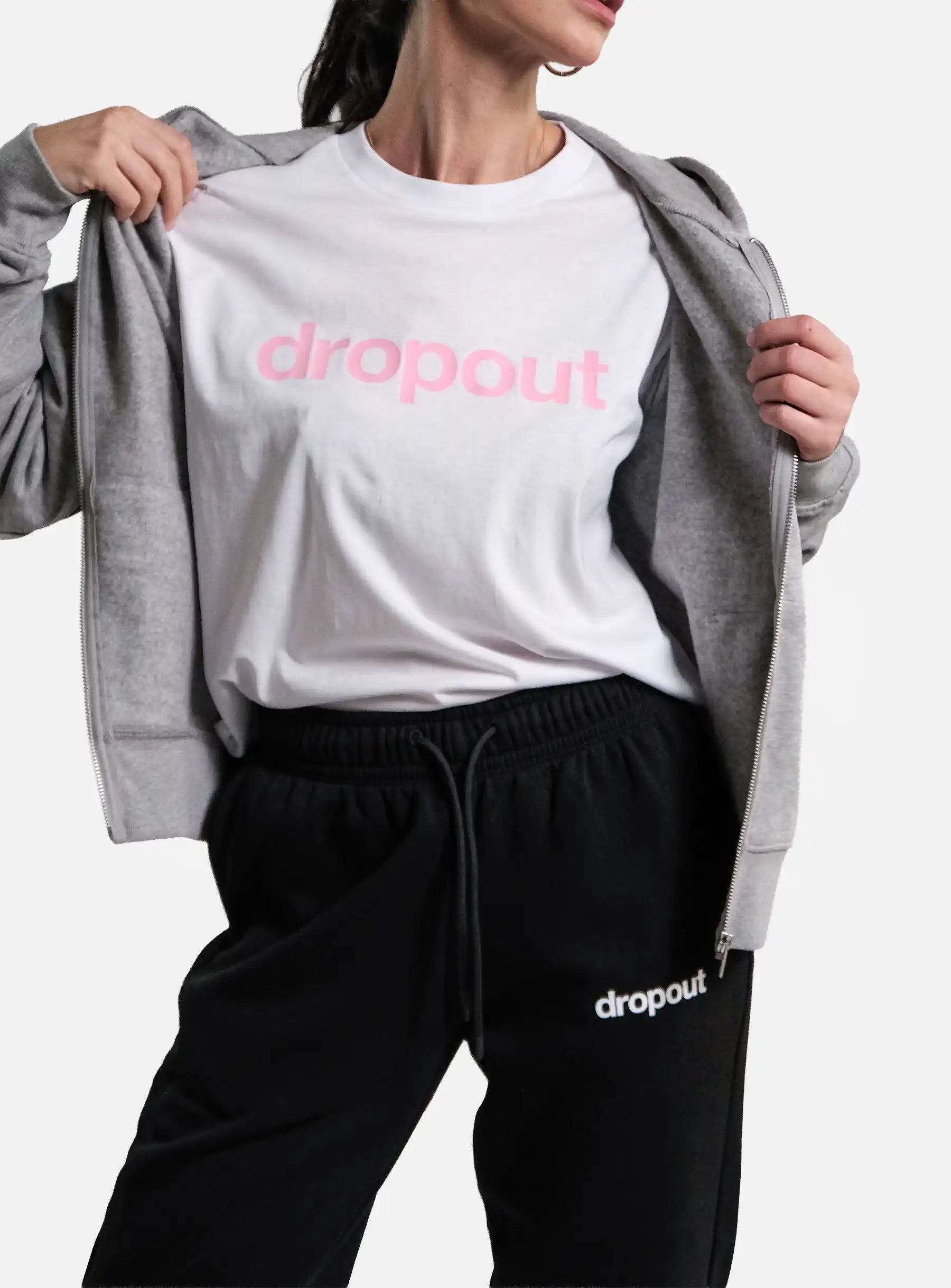 Person wearing a white 'dropout' t-shirt with a grey hoodie and black pants on a light grey background.