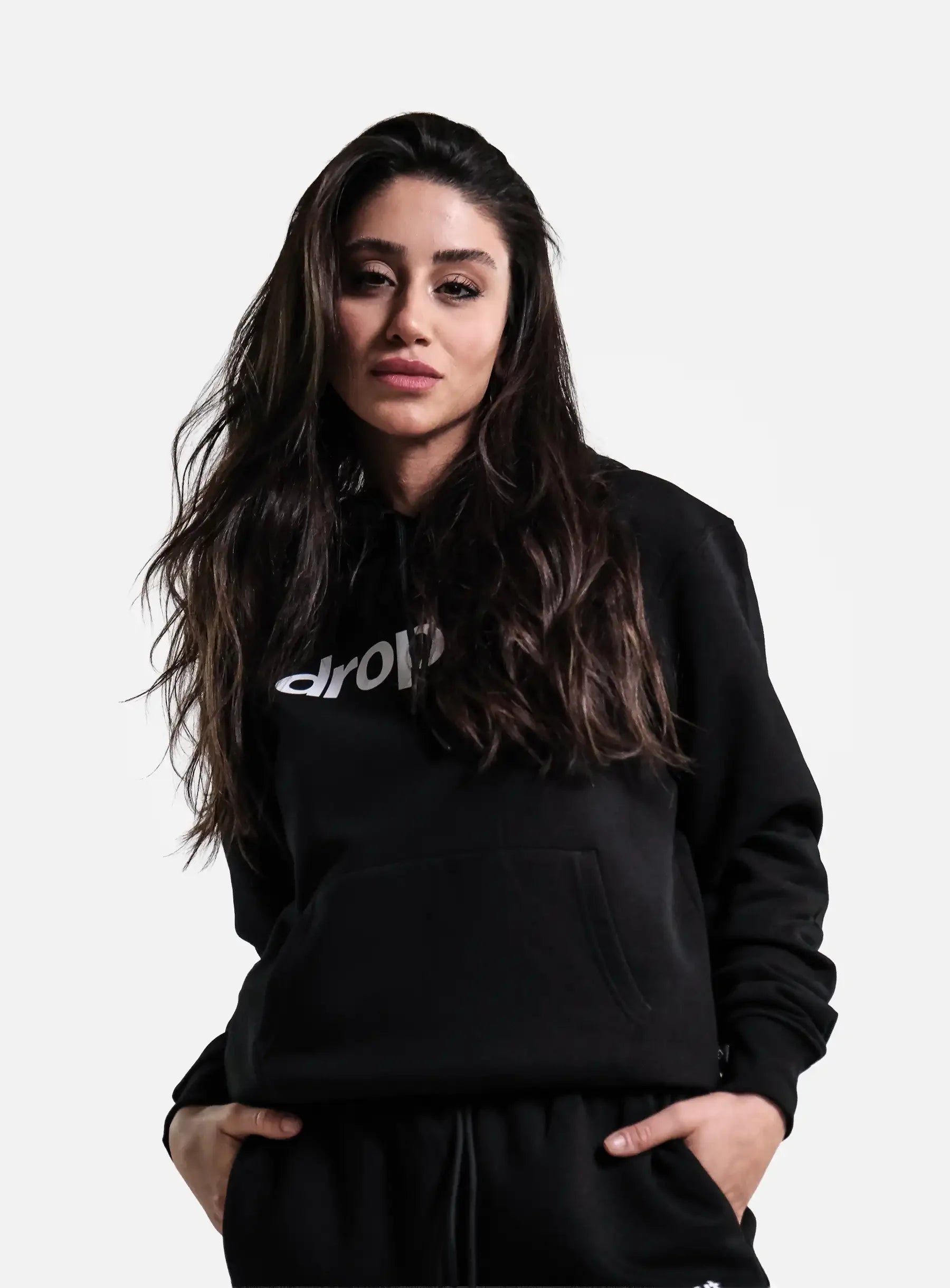 Woman wearing black streetwear hoodie with white text, hands in pockets, casual style
