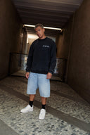 Casual street style: model wearing faded black dropout pencil sweatshirt with denim shorts and white sneakers.