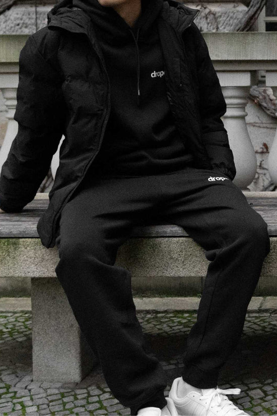 Person wearing a black hoodie and black sweatpants with 'dropout' logo sitting on stone steps.
