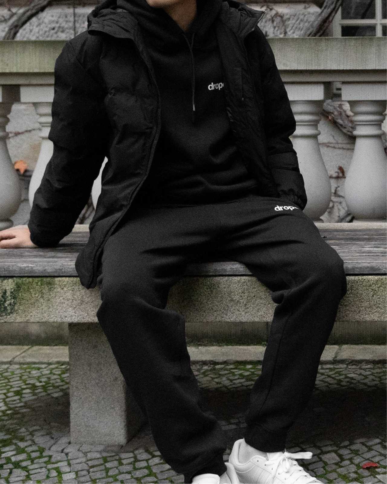 Person wearing a black hoodie and black sweatpants with 'dropout' logo sitting on stone steps.