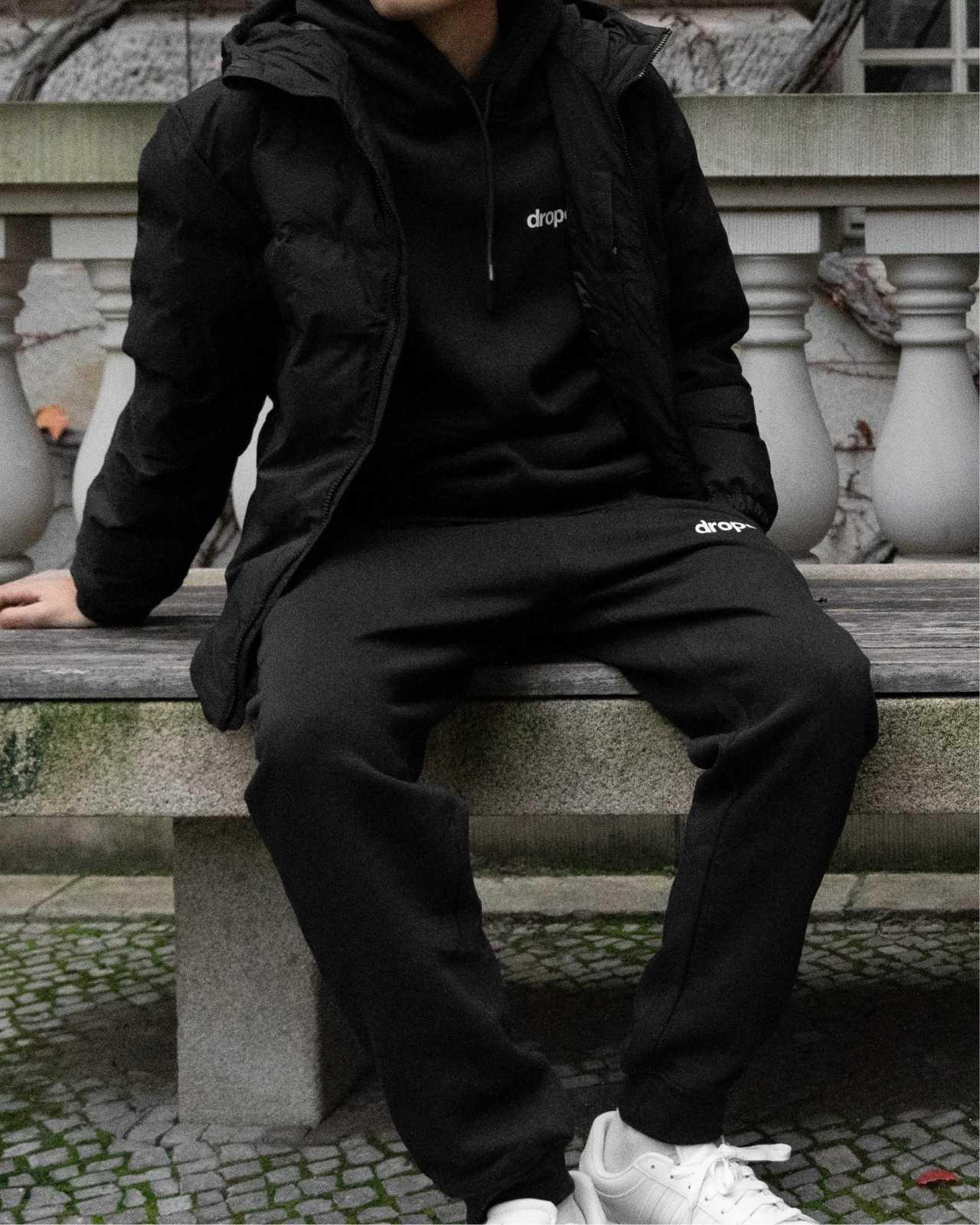 Person wearing a black hoodie and black sweatpants with 'dropout' logo sitting on stone steps.