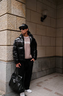 Person wearing a black puffer jacket and black pants standing against a tiled wall.